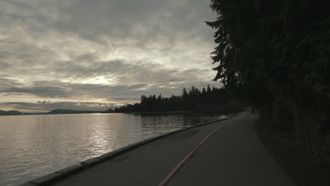Wide-backward-moving-shot-of-a-Stanley-Park-seawall-trail-in-dark-morning-atmosphere,-Vancouver,-Slowmotion