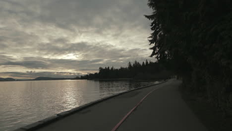 Amplia-Toma-En-Movimiento-Hacia-Atrás-De-Un-Sendero-Del-Malecón-De-Stanley-Park-En-Una-Atmósfera-Matutina-Oscura,-Vancouver,-Cámara-Lenta