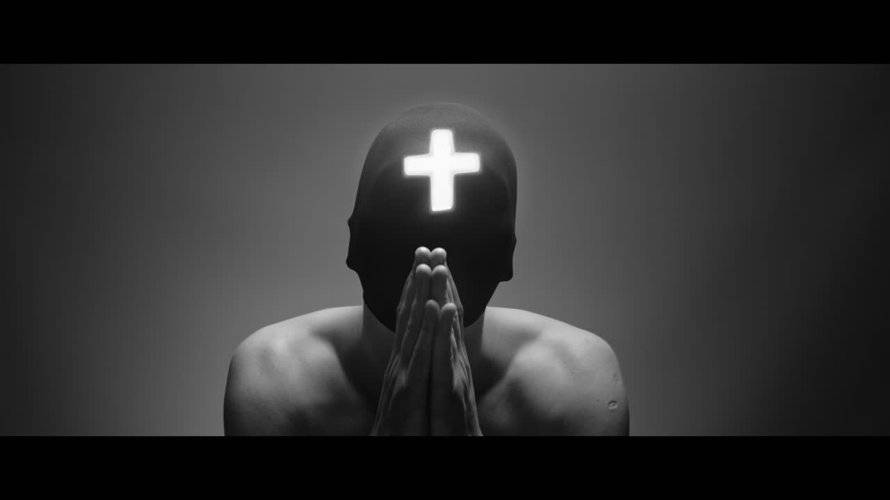 Masked and hooded man with cross of light glowing on his face looks in the camera