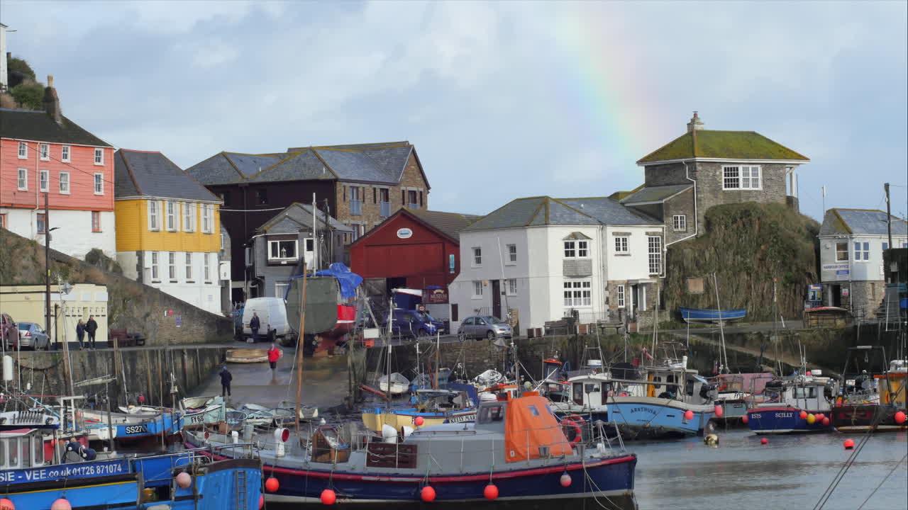 View looking across Mevagissey Harbour, rainbow above distant buildings, lifeboat sitting moored