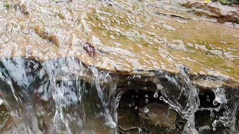 flowing waterfall from a mountain spring water stream running down huge sandstone slabs of rock with green moss, crystal clear drinking water, meditate tranquil and peaceful calm slow motion footage