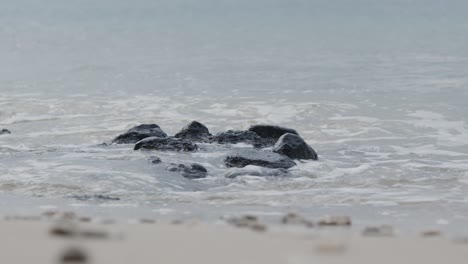 Piedras-Negras-En-La-Playa-Siendo-Engullidas-Por-Olas-Salpicando-Sobre-Ellas