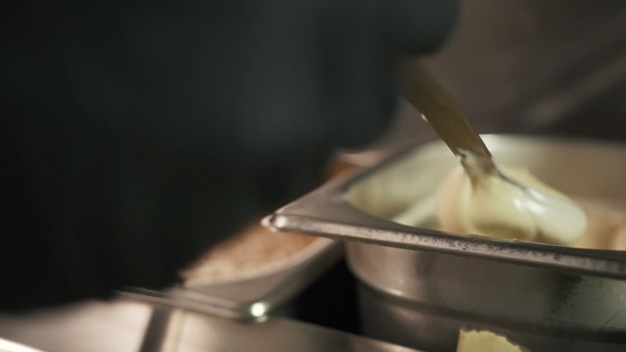 Close-up of hand wearing black glove takes white sauce from steel bowl. Rack focus