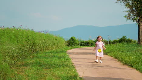 Una-Niña-Adorable-Camina-Hacia-Atrás-Por-La-Carretera-En-El-Parque-Montañoso-De-Las-Tierras-De-Cultivo-De-Anseong