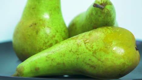 frische große grüne birnen drehen sich langsam auf einem schwarzen teller auf hellblauem hintergrund, gesundes ernährungskonzept, extreme nahaufnahme, kamera nach rechts drehend