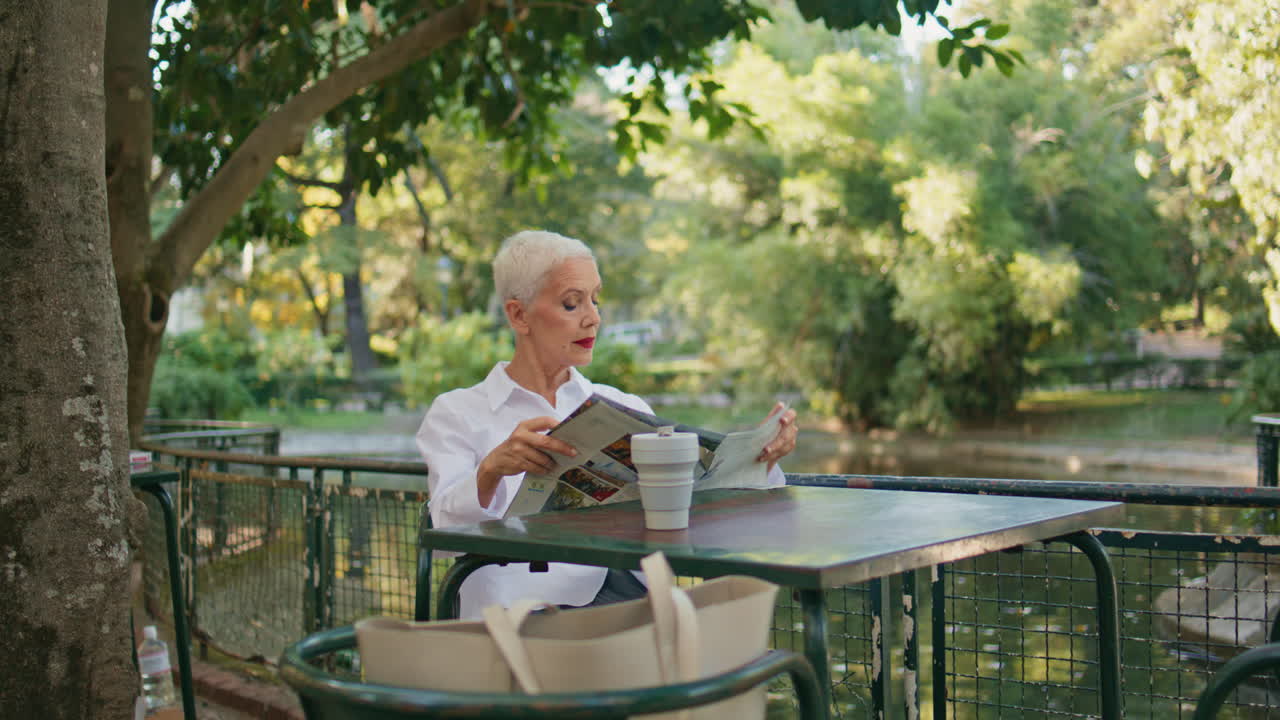 Signora anziana che tiene il giornale sulla terrazza di un caffè. Pensionata rilassata che si riposa al parco.