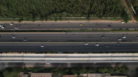 indian motorway in a cinematic aerial view showing fast-moving vehicles and metro railway bridge construction above the service road