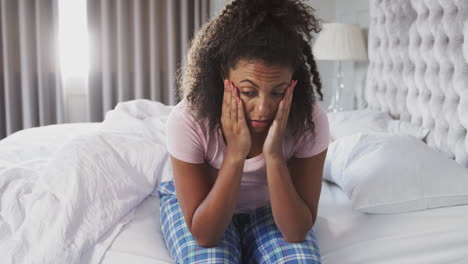 woman wearing pajamas suffering with depression sitting on bed at home