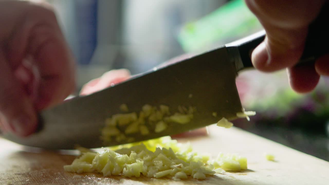 мужчина готовит ужин, нарезая чеснок и лук на кухонном столе
