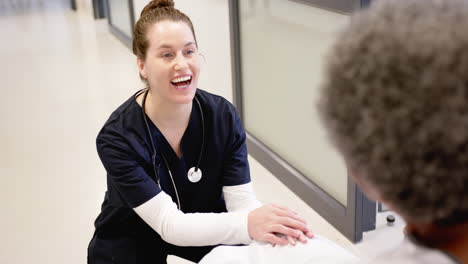 happy diverse female doctor talking with senior woman in wheelchair in hospital, slow motion