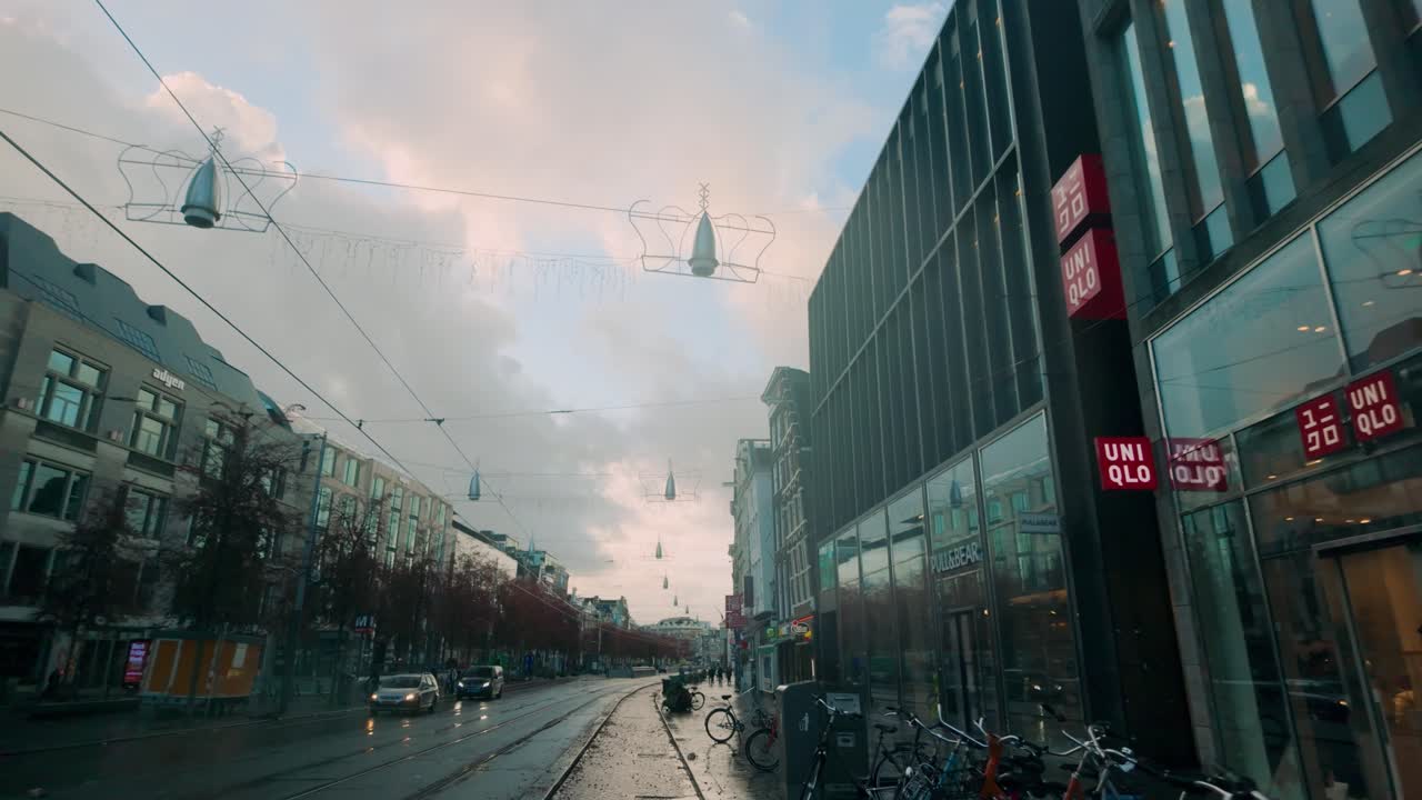 Rokin street in Amsterdam with tram tracks, modern and historic buildings, and shops under a vibrant morning sky. Bicycles line the sidewalk, capturing the city's iconic transportation culture