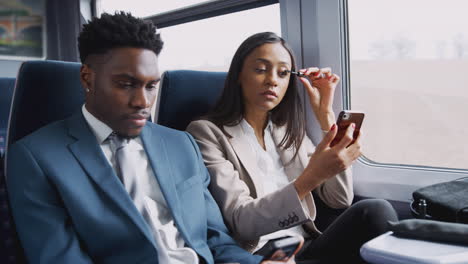 businesswoman sitting in train commuting to work putting on make up using mobile phone as mirror