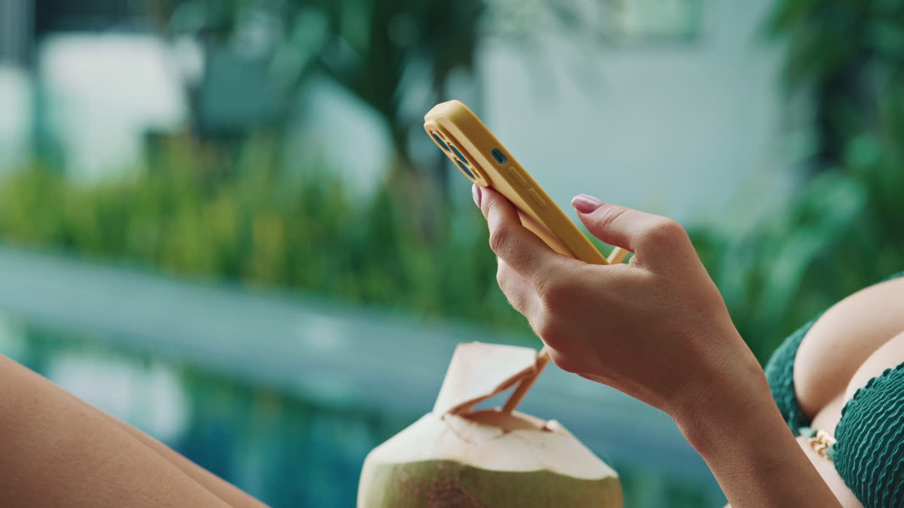 Woman relaxing by the pool with a coconut and phone