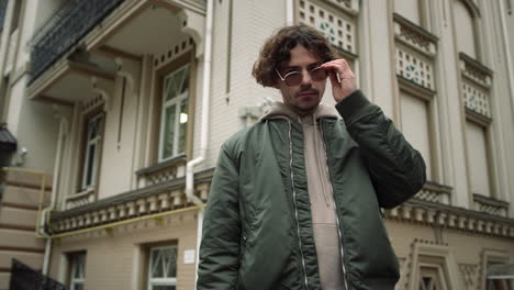 serious man looking camera outdoor. stylish hipster putting sunglasses on face.