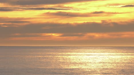 Golden-dawn-skies-over-calm-Mediterranean-Sea-reflecting-sunlight-on-waves,-seabirds-flying