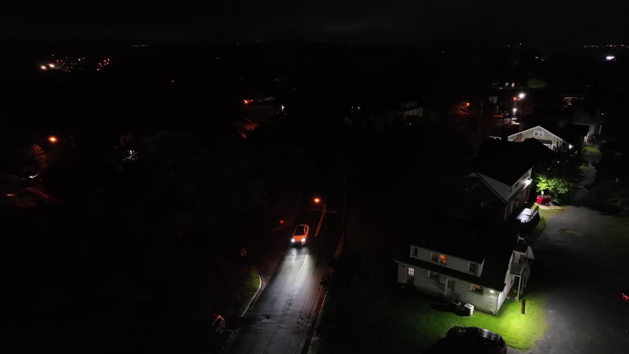 Car with headlight driving on road of american neighborhood at night. Aerial top down descend shot.