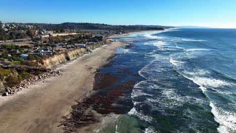 4K-Aerial-drone-shot-of-Beach-coastline-in-Cardiff-By-The-Sea-with-the-blue-Pacific-Ocean-with-waves-coming-in-and-beach-with-nice-houses-on-the-background