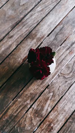 dark red carnations in white vase on wooden table