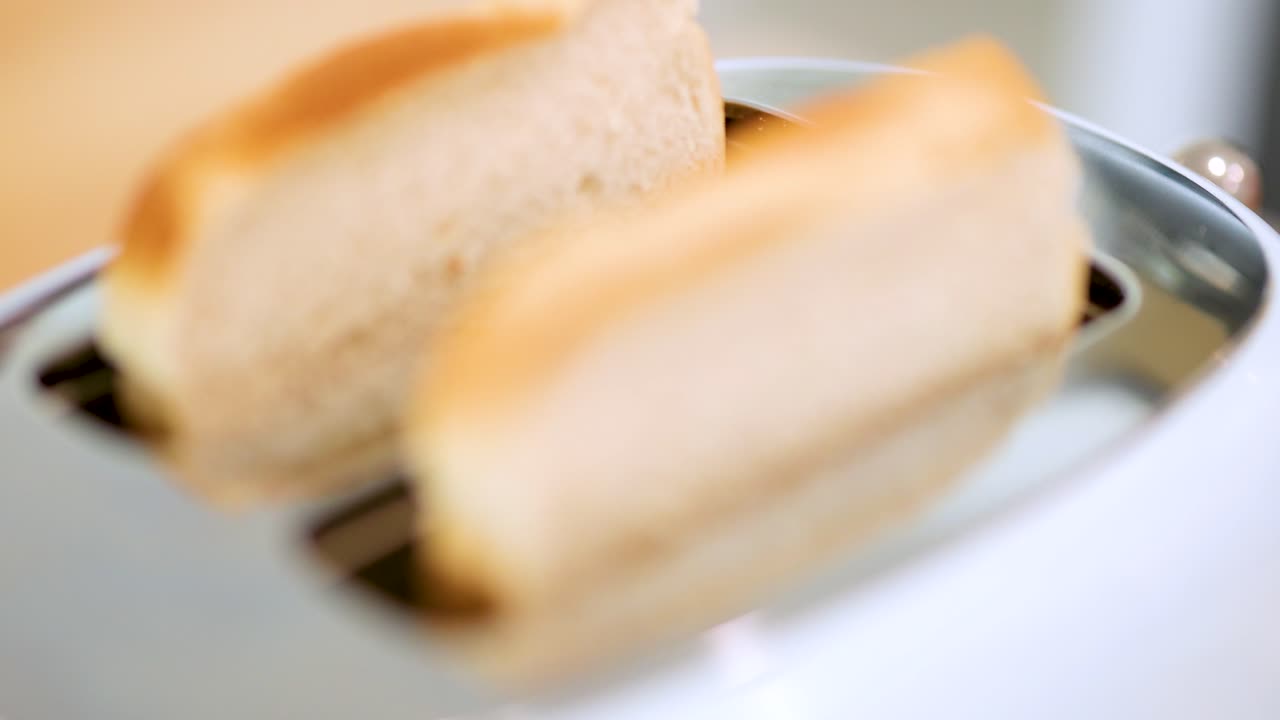 Two slices of bread rise from a stainless steel toaster in a bright kitchen, with glowing heating elements and shallow depth of field