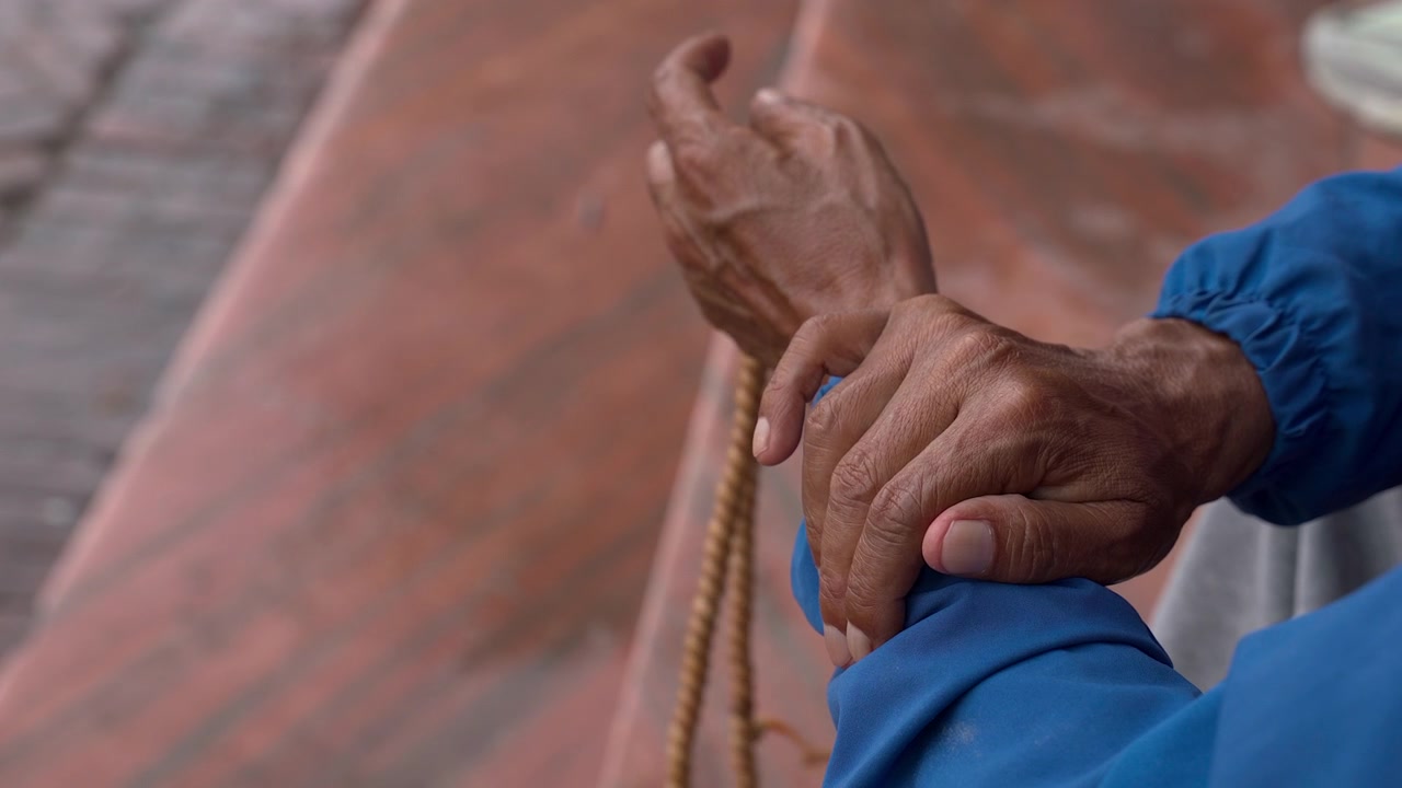 Lähikuva iäkkään henkilön käsistä, jotka pitelevät perinteisiä puisia mala-rukoushelmiä, heijastaen hiljaisen meditaation ja henkisen harjoituksen hetkeä Nepalissa.