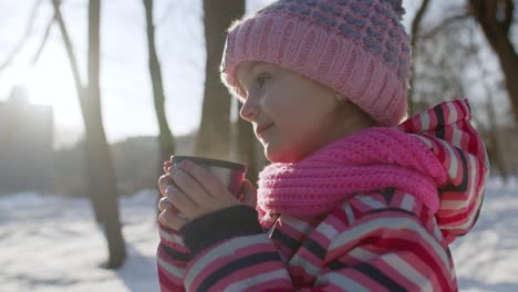 Lächelndes-Kind,-Mädchen,-Das-Heißen-Tee-Aus-Der-Tasse-Trinkt-Und-Versucht,-Sich-Im-Winterparkwald-Warm-Zu-Halten