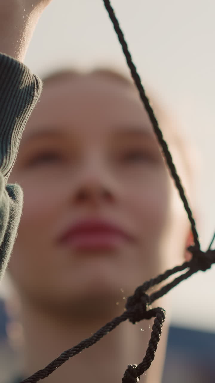 primer plano de una red de voleibol sostenida por alguien con un suéter verde, comprobándola con un cielo nebuloso en el fondo, centrándose en la red y las manos, la cara ligeramente borrosa