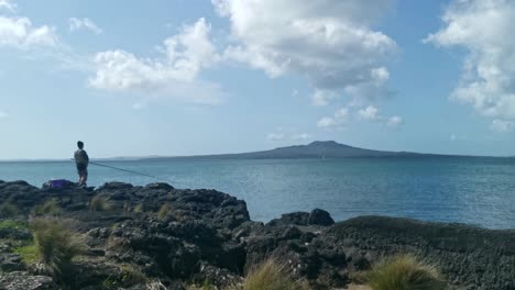 singular fisherman at thorne bay, new zealand with magnificent rangitoto volcano in the background