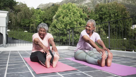 amigas afrodescendientes felices practicando yoga sentadas en el balcón, en cámara lenta.