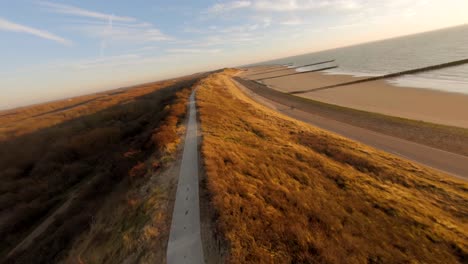 fast aerial shot of a high dune with a path on top of it during golden hour