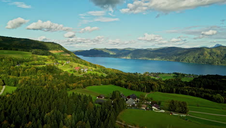 aerial capture of densely vegetated landscape with cluster settlements and a large water body visible in the background in attersee austria