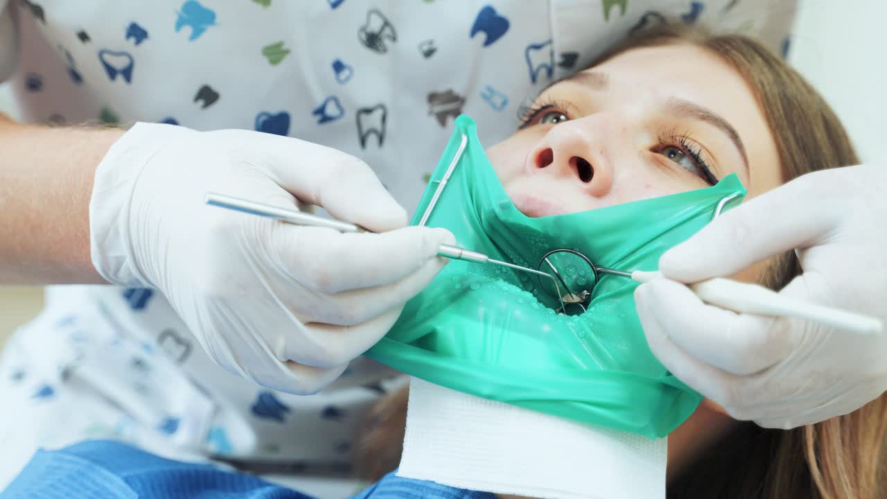 A doctor in white gloves treats a girl teeth to a patient. Inspection at the dentist using a mirror. Close-up