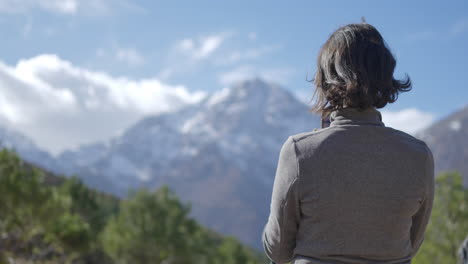 woman hiker taking pictures of a beautiful landscape with a blue sky, thick clouds, and a mountain summit covered in snow