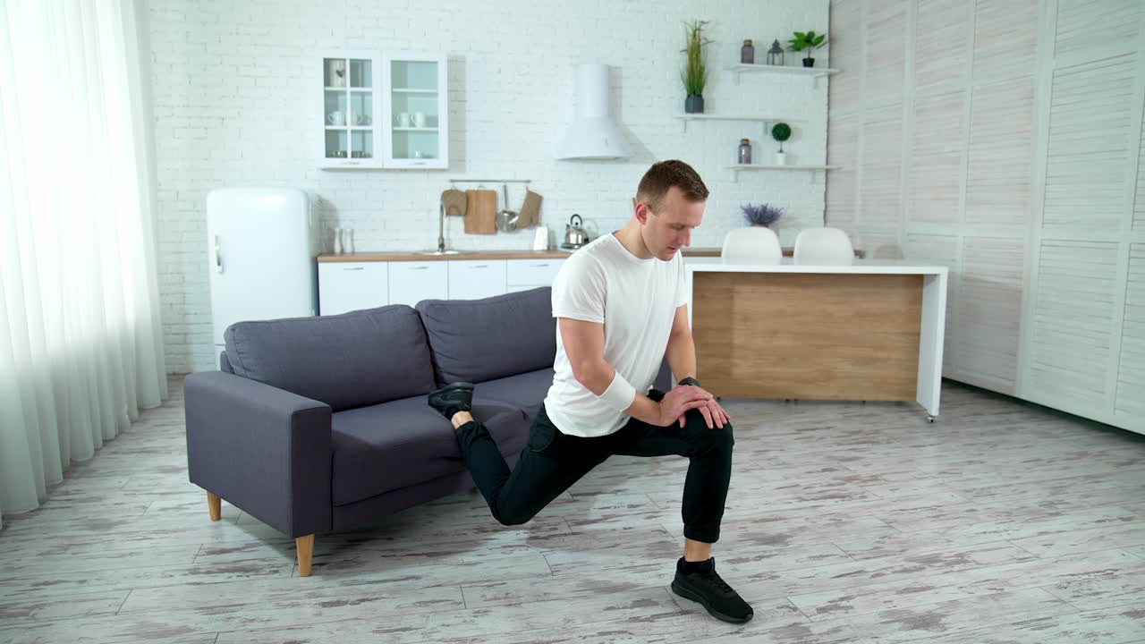 Young guy training in the kitchen. Active man doing exercises near the sofa at home. Isolation at home.