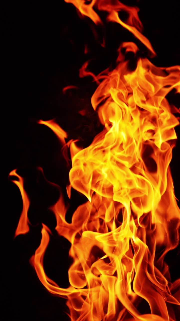 Beautiful fire flames moving in the darkness. Multiple sparks fly up and smoke rises behind. Close up. Vertical video