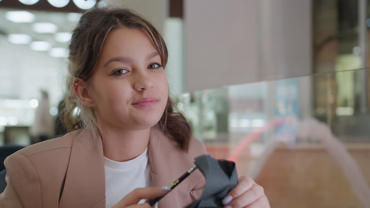 happy girl unboxing, cheerful young woman excitedly examines new makeup item at shopping mall, joyful female shopper shows delighted expression while unveiling recent beauty purchase in mall