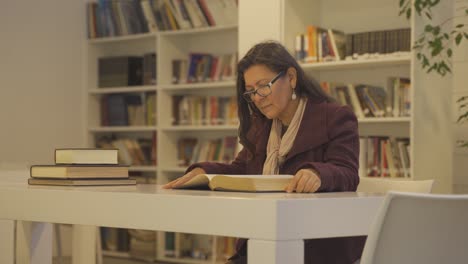 Middle-aged-women-is-sitting-at-desk-in-big-library-rewriting-text-from-book