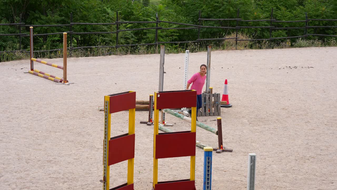 Mentre allestisce gli ostacoli per il salto a cavallo, una donna felice sta parlando con un'altra persona
