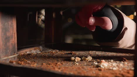 vista parcial de primer plano de la mano dejando caer alimento para las aves dentro de la casa de pájaros de madera con partículas de alimento en el suelo, vida silvestre al aire libre alimentándose por la noche en el parque de invierno con luces bokeh borrosas