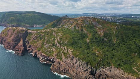 a drone soars above the craggy cliffs of signal hill, revealing a green headland with steep drops into the atlantic and glimpses of st. john’s harbour in the distance