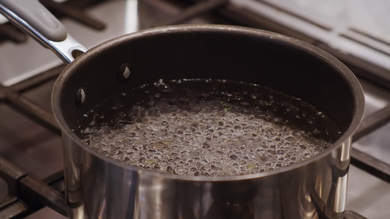 A stainless steel pot filled with freshly boiling water. Bubbles rise to the top of the pot. Heating up the water in preparation for cooking on a modern kitchen stove. Shot in slow motion