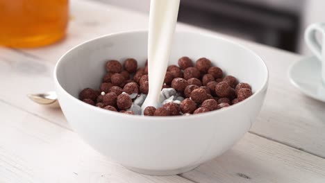 pouring milk to white bowl full of chocolate ball-shaped cereals in slow motion