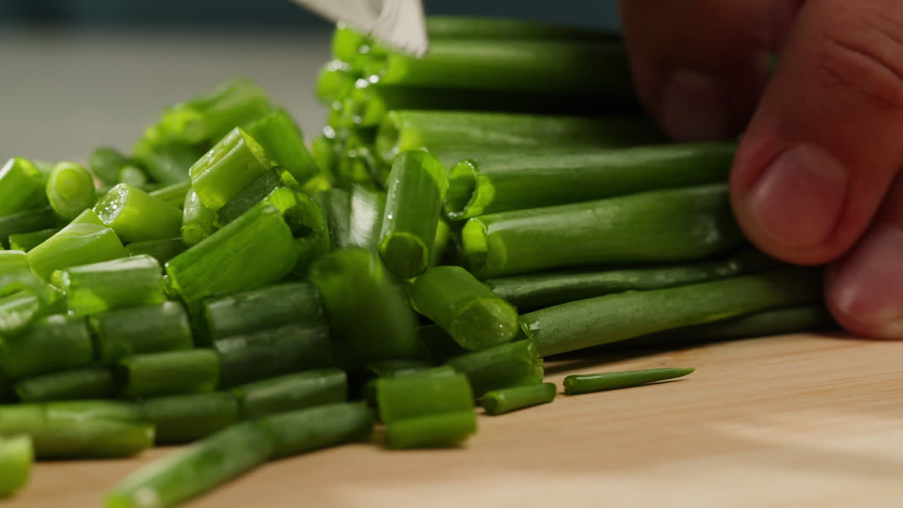 Cutting fresh green onions on a cutting board, close up chef cooking green vegan salad.