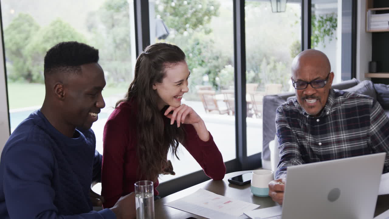 Happy diverse couple and male financial advisor using laptop and discussing at home,slow motion