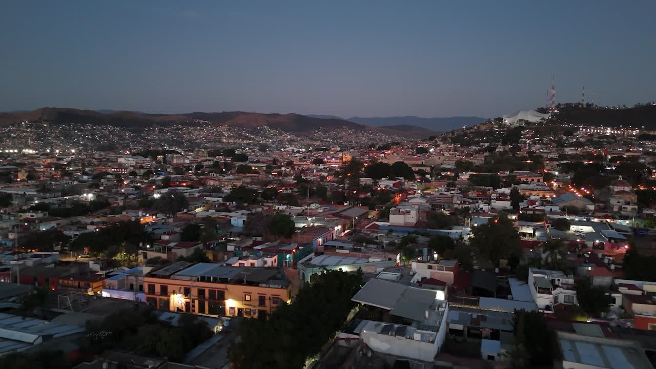La vista aerea da drone cattura una città vivace al crepuscolo, con i colori del tramonto che illuminano le silhouette delle montagne, le luci scintillanti della sera e un paesaggio urbano tentacolare sotto un cielo spettacolare