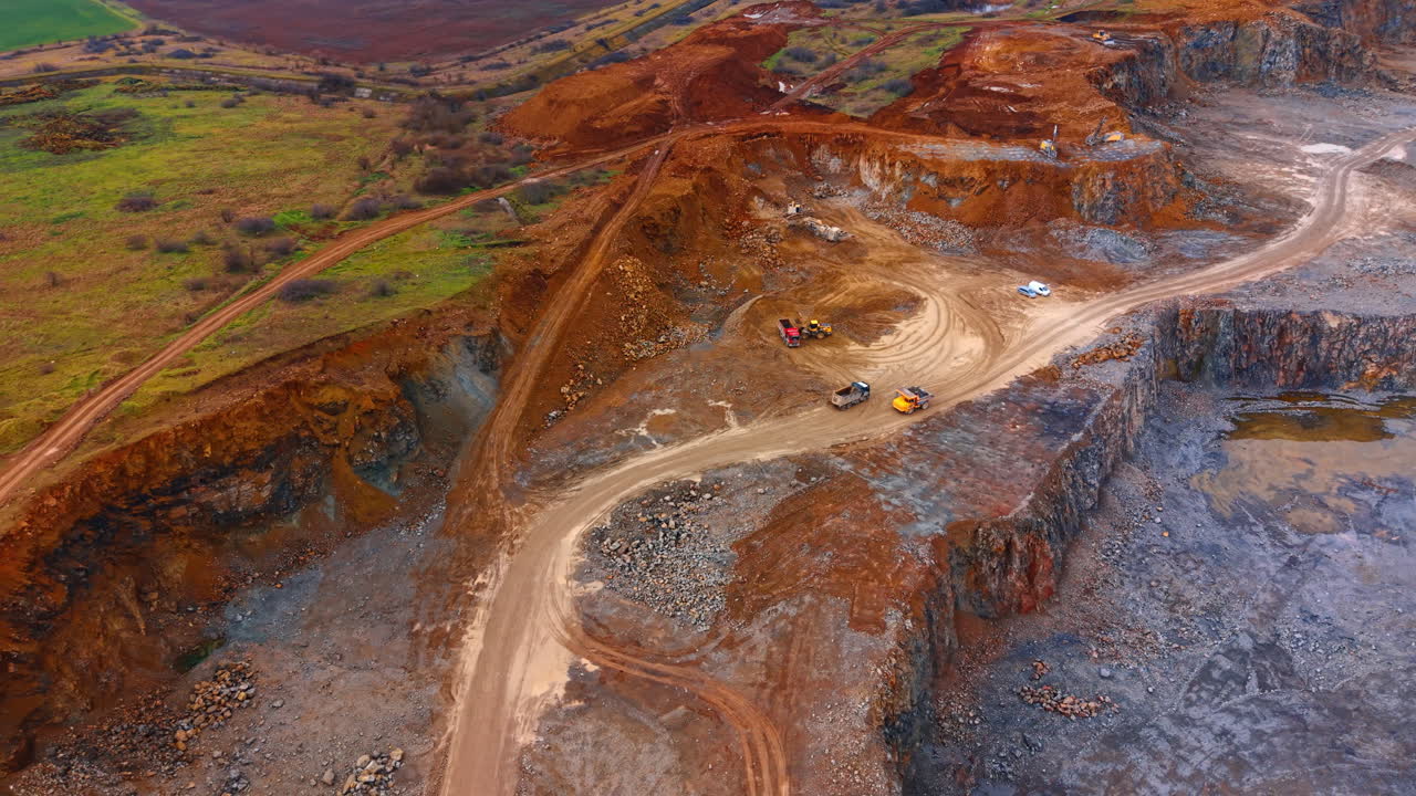 High angle view of red earth and rock quarry. Aerial perspective of a quarry section with reddish soil, tracks, and yellow heavy machinery
