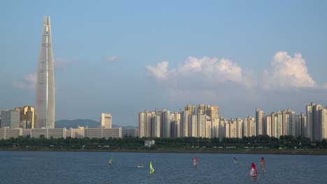 un grupo de hombres practica windsurf en el río han cerca de la torre lotter durante el día, distrito jamsil de la ciudad de seúl, corea del sur
