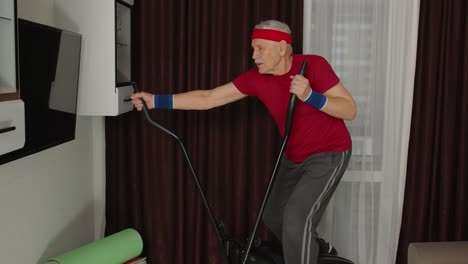 hombre mayor en ropa deportiva usando orbitrek en la sala de estar haciendo entrenamiento deportivo ejercicios cardio en casa