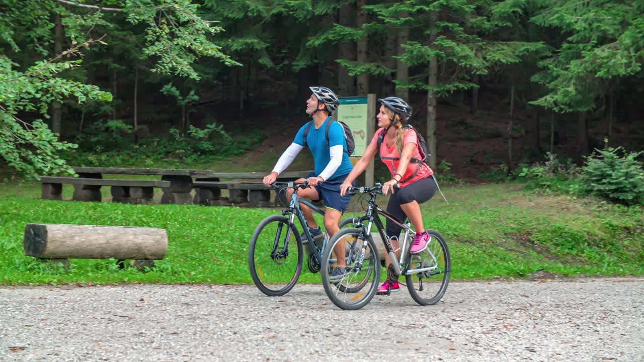 Couple ride bicycles on gravel pavement, point up, Slovenia, real time