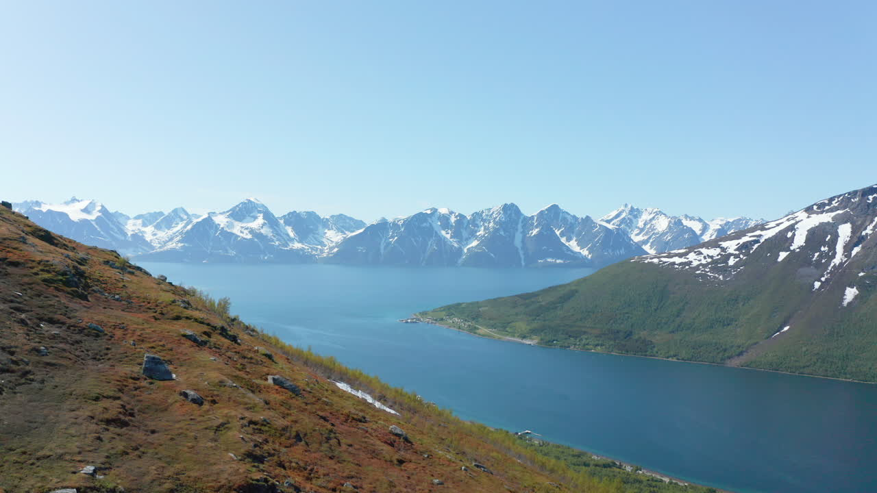 aéreo, creciente, tiro de drone con vista al mar de barents y las montañas nevadas del fiordo lyngenfjord, soleado, día de verano, en rotsund, nordland, noruega