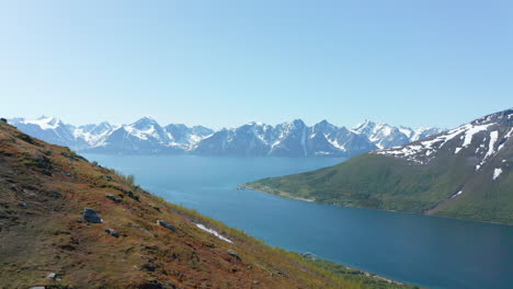 Aerial,-rising,-drone-shot-overlooking-the-Barents-sea-and-the-snowy-mountains-of-the-Lyngenfjord,-sunny,-summer-day,-in-Rotsund,-Nordland,-Norway